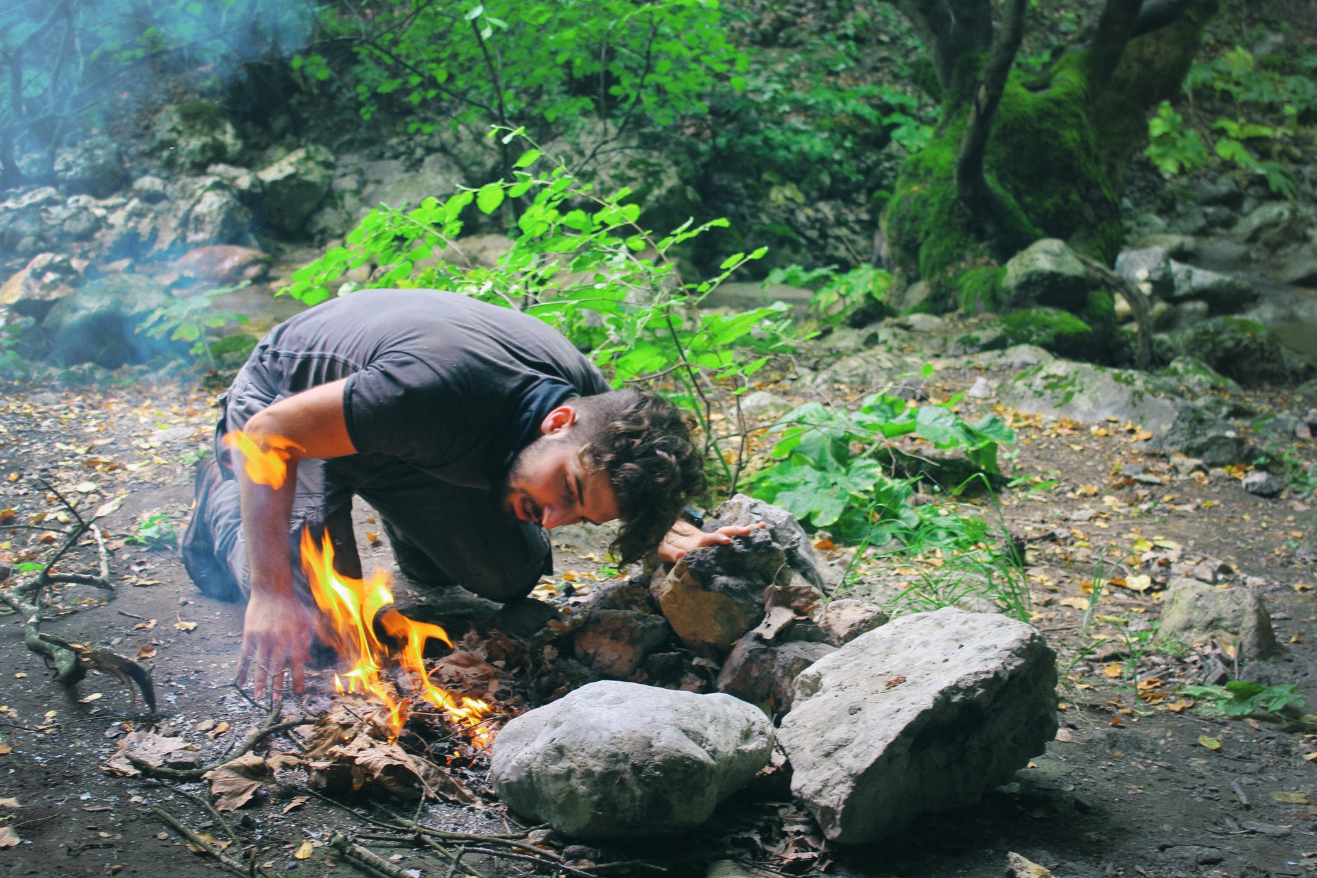 A person leaning down next to some rocks as they start a fire while survivalist camping.