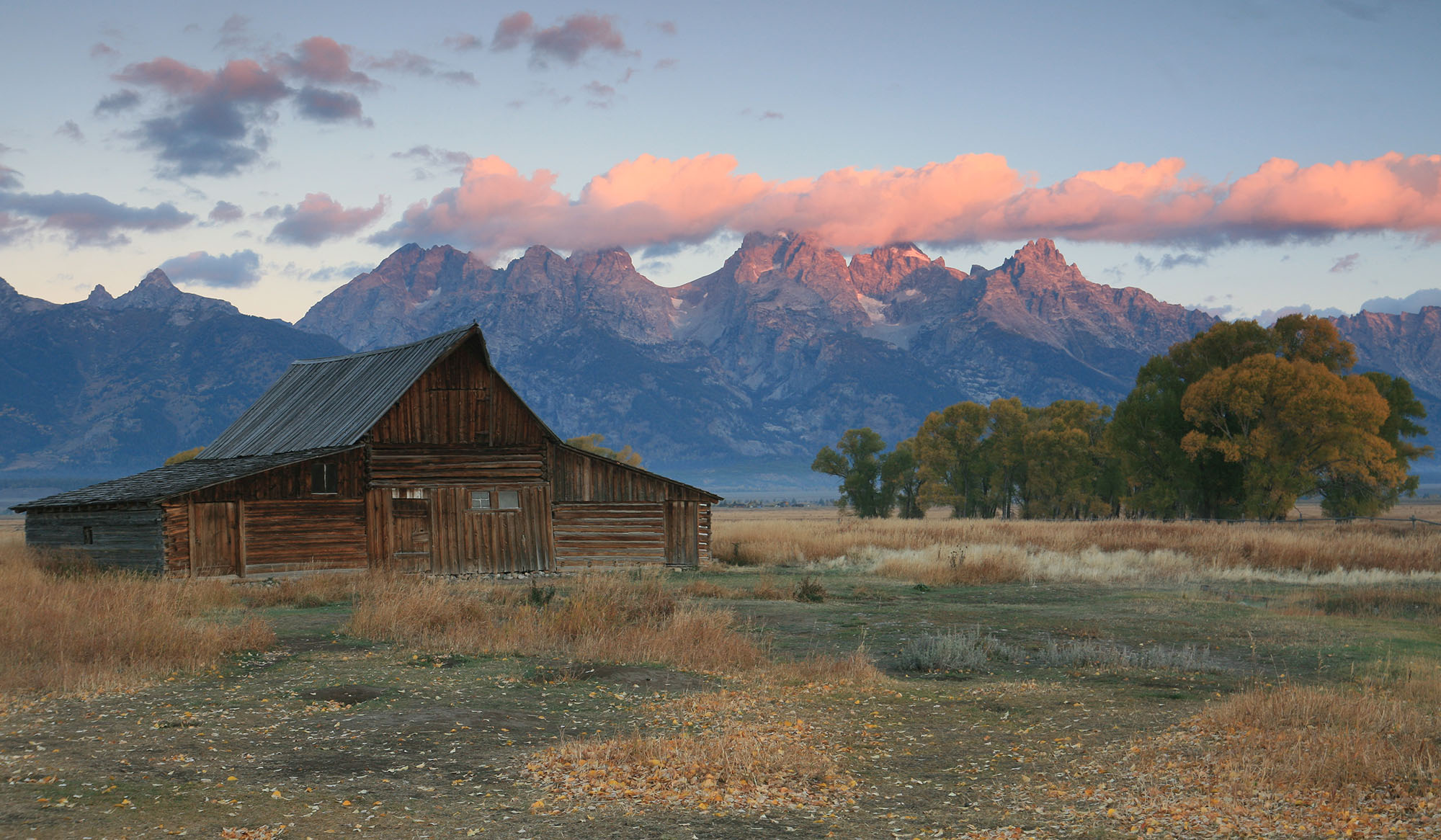 An old wood farmhouse in a valley in front of a mountain range.